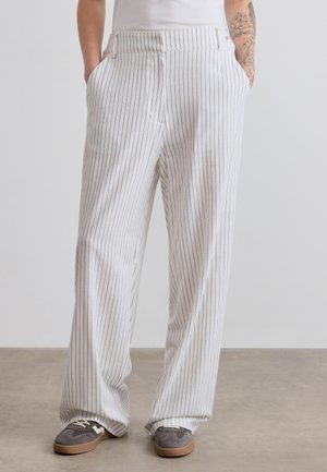 Wide-leg trousers in white fabric with thin black vertical stripes, featuring side pockets and a relaxed fit. Paired with gray sneakers.