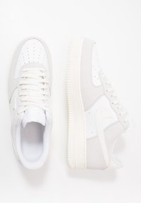 Nike Air Force 1-sneakers i vitt och ljust grått mocka och läder. Har perforerad tå, platta snören och texturerad gummisula.