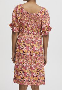 Kwiatowa sukienka na różowym tle, zdobiona żółtymi i białymi kwiatami. Marszczony gorset i krótkie falbaniaste rękawy. Długość do kolan.