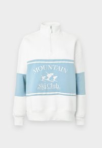 Valge ja helesinine pusa kõrge krae, tõmblukuga ning suusateemalise graafikaga. Omab värvilahenduse plokki ja soonikkoes mansette.