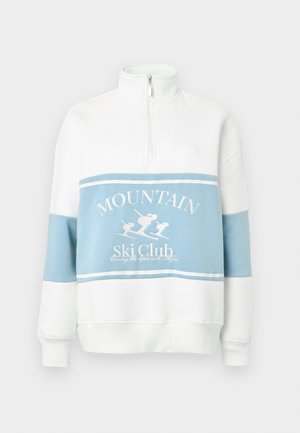 Biała i jasnoniebieska bluza z wysokim kołnierzem, zamkiem błyskawicznym i grafiką o tematyce narciarskiej. Posiada blokowy wzór kolorystyczny oraz ściągacze przy rękawach.