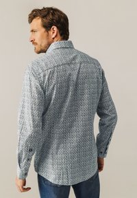Herren Langarmhemd in Hellblau mit filigranen dunkelblauen Mustern, ausgestattet mit einem spitzen Kragen und Knopfmanschetten, aus gewebtem Stoff gefertigt.