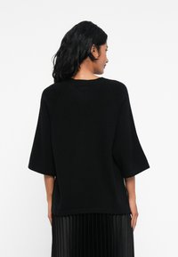 Pull noir oversize avec des manches courtes et un col rond, fabriqué à partir d'un matériau doux. Présente une coupe décontractée, sans motifs ni embellissements.