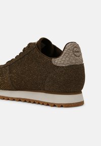 Baskets marron texturées avec une semelle blanche et un patch de talon en peau de serpent beige, montrant les détails arrière et latéraux.