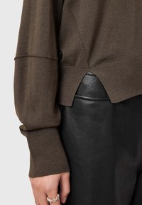 Brązowy sweter dziany z prążkowanymi mankietami i bocznymi rozcięciami, zestawiony z dopasowanymi czarnymi skórzanymi spodniami. Widoczne są wyraźne faktury i czyste linie.