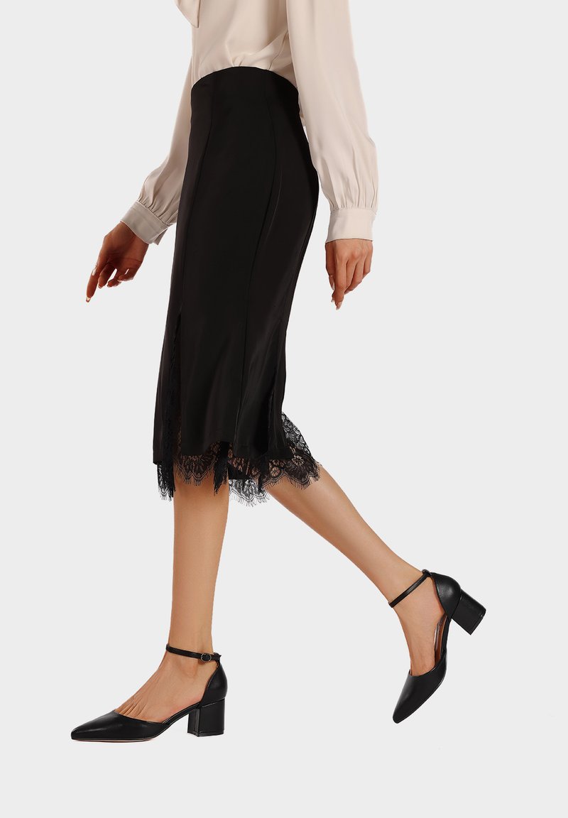 Scarpe con tacchi alti neri, con punta affusolata e cinturino alla caviglia. Finitura in pelle liscia, con tacco a blocco e design elegante. Dettaglio in pizzo sull'orlo della gonna.