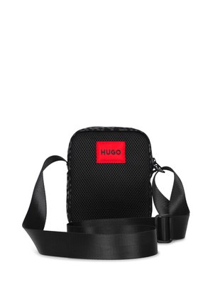 Sac bandoulière en mesh noir avec une sangle réglable et un patch rouge marqué HUGO à l'avant, isolé sur fond blanc.