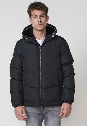 Chaqueta de plumas negra con cierre de cremallera, con capucha forrada de forro polar y detalle de logo en el cuello y la manga, textura acolchada.