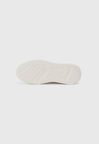 Fehér sneaker talp bordázott textúrával, hullámos mintázattal és a középen kiemelkedő "GUESS" márkanevével.