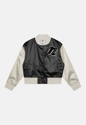 Chaqueta bomber de satén negra y crema con cierre de botones, puños acanalados y el logo de "Nike" bordado en blanco en el lado izquierdo del pecho.