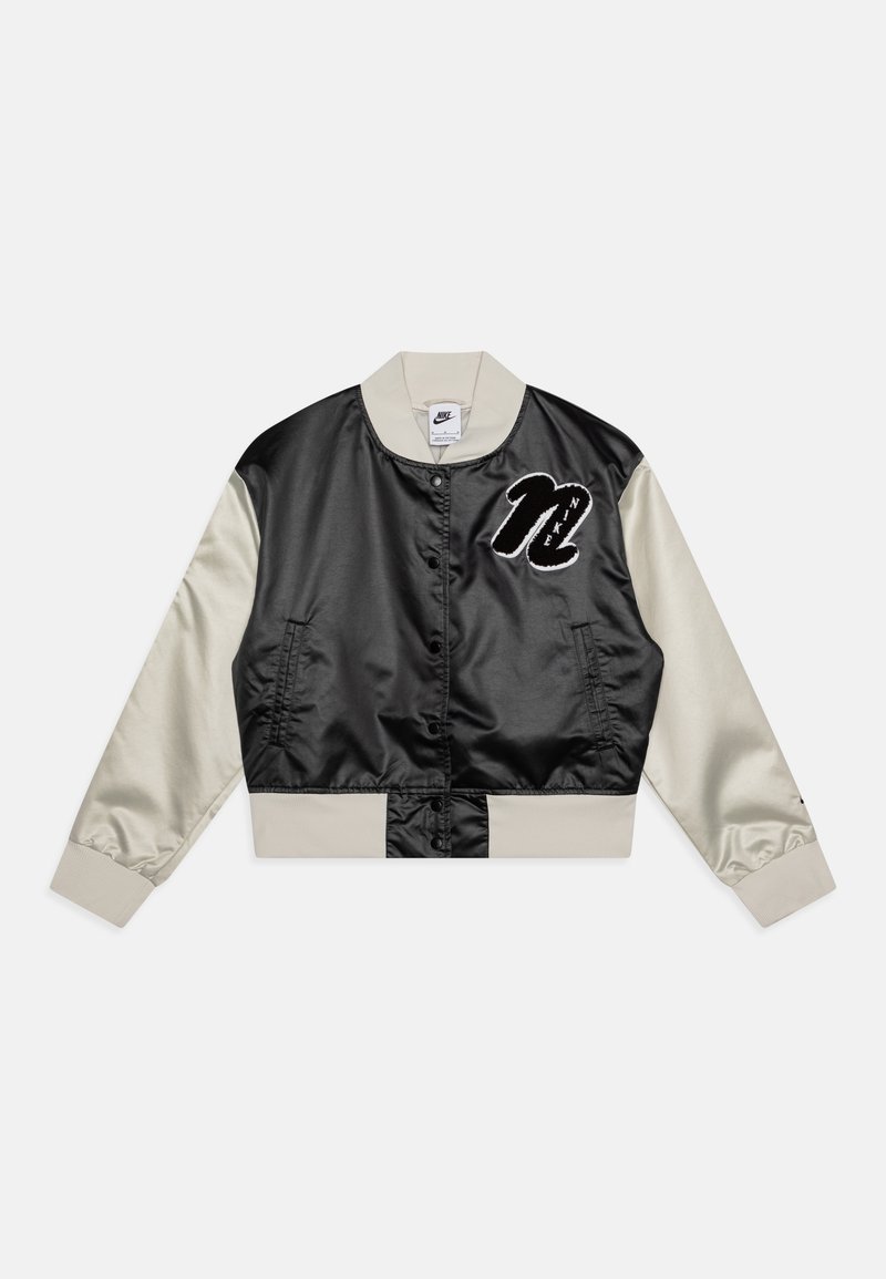 Chaqueta bomber de satén negra y crema con cierre de botones, puños acanalados y el logo de "Nike" bordado en blanco en el lado izquierdo del pecho.