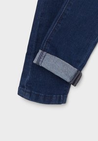 Vaqueros de mezclilla azul oscuro con un dobladillo enrollado en un tono azul más claro. Presentan costuras cosidas y un acabado texturizado, que muestran un tejido duradero.