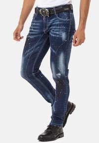 Slim-fit blauwe denim jeans met verfspetters in rood, wit en groen. Voorzien van een riem met een gestructureerde zwarte afwerking en een zilveren gesp.
