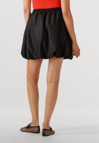 Zwarte, opbollende mini-jurk met een gestikte tailleband, met een gladde textuur. Gecombineerd met geweven platte schoenen in zwart en goud.