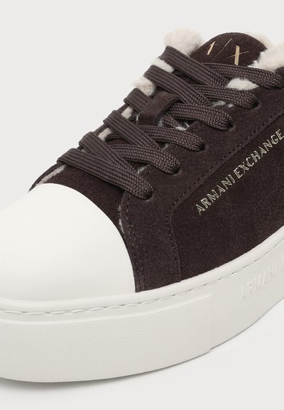 Baskets en daim marron foncé avec semelle blanche épaisse en caoutchouc et bout renforcé, lacets marron et logo "ARMANI EXCHANGE" sur le côté.