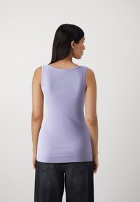 Top senza maniche di colore viola chiaro, realizzato in tessuto elasticizzato; presenta un colletto rotondo e un design senza cuciture sul retro. Abbinato a jeans scuri.
