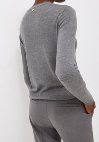 Maglione grigio lavorato a maglia con scollo smerlato e piccolo dettaglio con bottone rotondo sul retro. Tessuto morbido e design aderente.