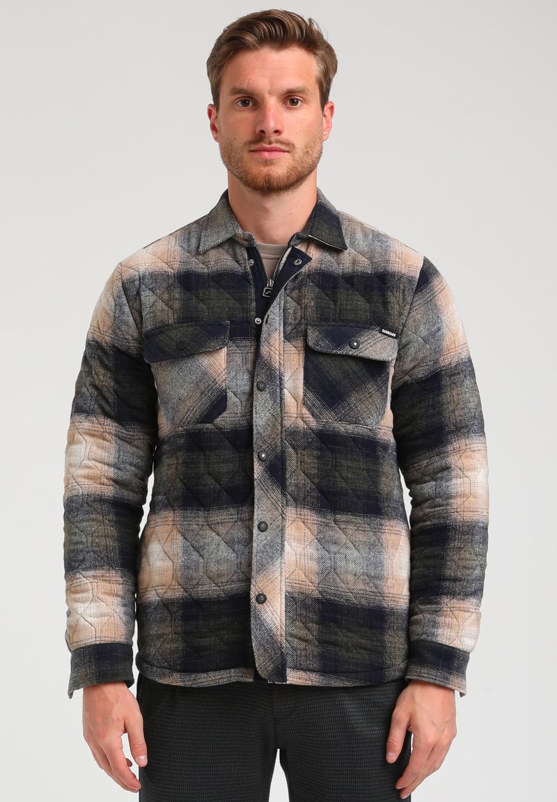 Gequilte flanellen shirt in marineblauw, tan en grijs ruitpatroon. Voorzien van twee borstzakken en knoopsluiting. Zachte textuur met een gestructureerde pasvorm.