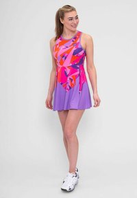 Robe de sport violette et rose avec des motifs géométriques, sans manches, avec une jupe évasée et un col rond. Portée avec des baskets blanches.