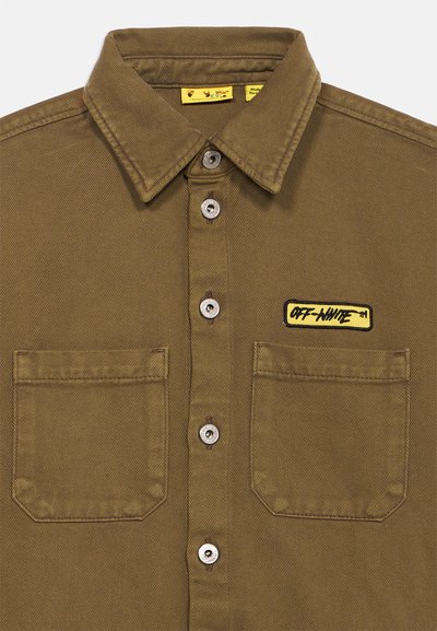Καφέ πουκάμισο με κουμπιά και δύο τσέπες στο στήθος, με ένα κίτρινο ορθογώνιο λογότυπο "Off-White" στην δεξιά τσέπη.