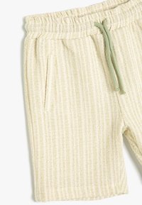 Helle beige Shorts aus strukturiertem Stoff, mit einem elastischen Bund und grünem Kordelzug sowie Seitentaschen.