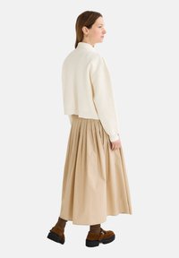 Pull en cream à manches courtes avec un col rond, associé à une jupe plissée beige. Des bottes brunes à talon épais complètent la tenue.