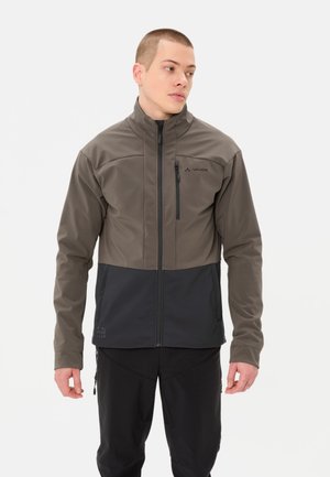Mann trägt eine zweifarbige graue Softshelljacke mit Frontreißverschluss und Brusttasche, steht vor einem einfarbigen Hintergrund und schaut zur Seite.