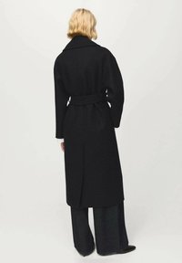 Lange zwarte wollen jas met een brede kraag, een getailleerde taille met ceintuur en een rechte pasvorm met een centrale achtersplit.