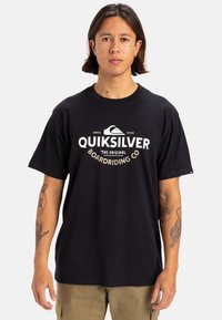 Camiseta de algodón negra de manga corta, con un logotipo gráfico blanco en el frente. El diseño incluye una montaña y detalles de texto.