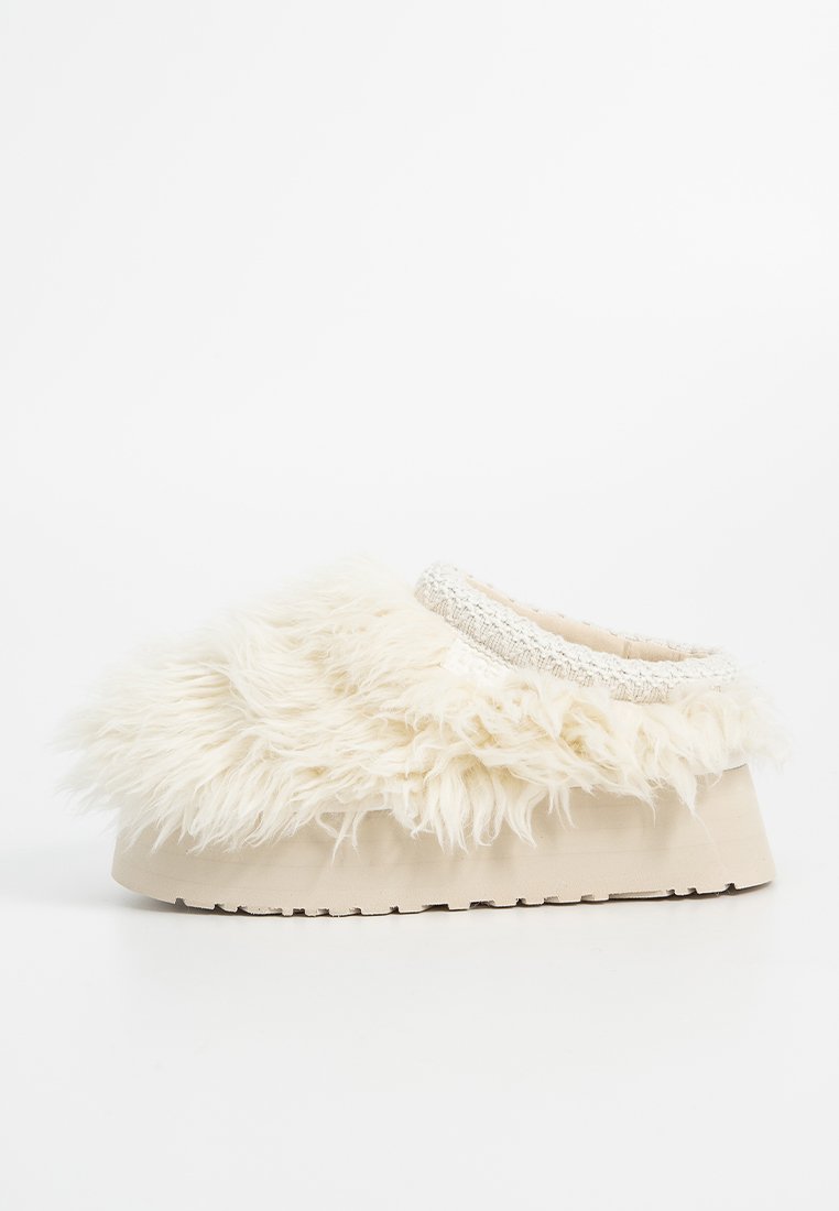 Pantofole bianche soffici con una parte superiore in pelliccia sintetica testurizzata, suola color crema e un bordo intrecciato attorno all'apertura per un tocco di dettaglio in più.