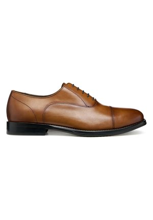 Zapato Oxford de cuero marrón para hombre con cierre cerrado, puntera de capitán y suela negra, mostrado desde el lado izquierdo sobre un fondo blanco.