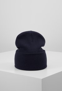 Bonnet en tricot bleu marine avec une texture côtelée, présentant un revers replié et un design ample sur le dessus.