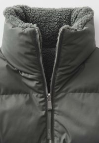 Daunenjacke mit einem dunkelgrünen Außenmaterial, flauschigem grauen Innenfutter, hohem Kragen und silbernem Reißverschluss. Verfügt über ein strukturiertes Stoffdesign.