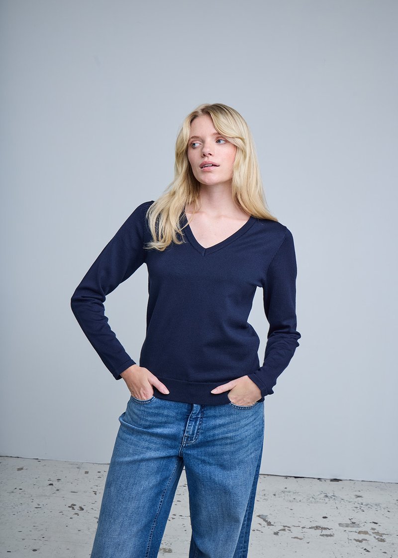 Pull col en V bleu marine en tissu tricoté lisse, avec manches longues et ourlet côtelé, associé à un jean large couleur bleu clair.