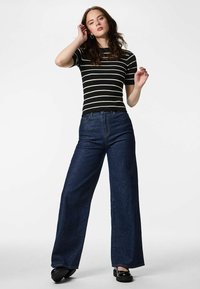 Crno-bijela prugasta rebrasta majica uparena s tamnoplavim trapericama širokih nogavica s visokim strukom. Crne masivne cipele upotpunjuju izgled.