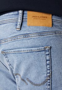 Ljust blå denimjeans med en läderlapp märkt "JACK & JONES." Har synlig sömnad och två bakfickor. Strukturerad tyg.