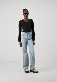 Svart topp med teksturerte puffermer, slitte blå jeans og chunky kremfargede joggesko. Tilbehør inkluderer solbriller og et kjedehalskjede.