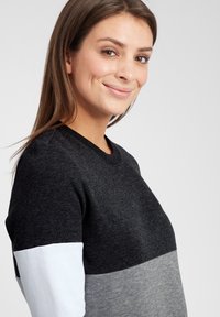 Genser laget av bomullsblanding med ribbet halslinning, svart overdelsseksjon og fargeblokkerte paneler i grått og hvitt. Myk, teksturert finish.