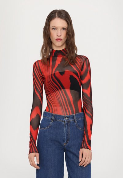 Body din plasă cu mânecă lungă, îmbrăcat cu modele roșii și negre în spirală, guler înalt și un design ajustat, asortat cu blugi din denim cu talie înaltă.