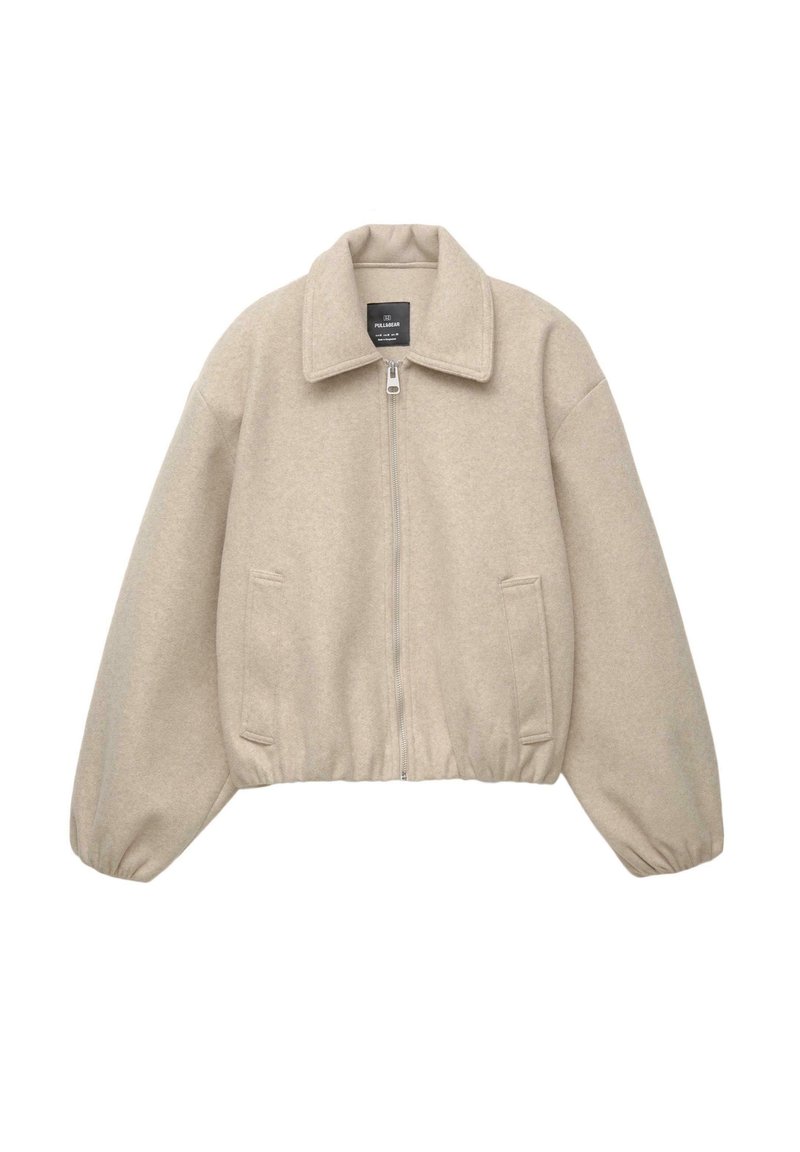 Beige kort jacka med dragkedja, bred krage och elastiska ärmslut. Tillverkad av mjukt tyg med två framfickor.