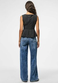Top peplum noir avec une silhouette ajustée et une texture douce, associé à un jean en denim bleu à jambes larges présentant un délavage et des poches arrière.