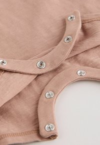 Gros plan sur un tissu beige avec des boutons-pression argentés partiellement ouverts sur deux bords de vêtement se chevauchant.