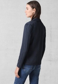 Blazer blu navy a righe sottili con una vestibilità su misura, colletto a punta e maniche lunghe, abbinato a jeans blu per un look casual.