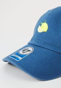 Casquette de baseball bleue en coton, avec des broderies de citrons et de limes jaunes à l'avant et un patch circulaire de marque sur le côté.