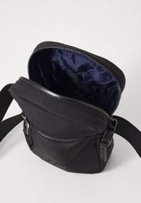 Borsa a tracolla nera realizzata in tessuto resistente, dotata di chiusura con zip, tracolla regolabile e un interno liscio con fodera blu navy.