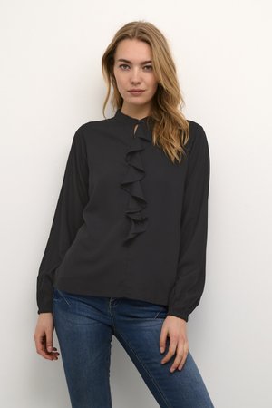 Blusa nera in tessuto leggero con dettagli arricciati frontali, colletto alto e maniche lunghe. Abbinata a jeans blu.