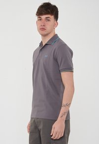 Polo grigio a maniche corte, con accenti blu e verdi sul colletto e sulle maniche, dotato di un piccolo logo ricamato sul petto.