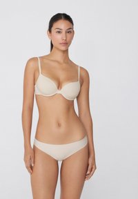 Beiger, gepolerter BH mit verstellbaren Trägern, nahtlosen Körbchen und passendem, niedrig sitzendem Bikini. Glatte Textur und minimalistisches Design.