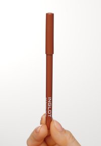 Crayon rétractable marron avec une texture lisse et une finition mate, étiqueté "INGLOT" en blanc. Tenue entre les doigts contre un fond clair.