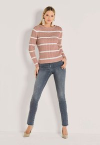 Rosa Strickpullover mit weißen Streifen, gerippter Textur und rundem Halsausschnitt, kombiniert mit blauen Skinny-Jeans und beigen Absatzschuhen.